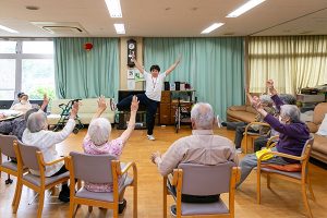 施設内でのレクリーション活動。入居者が椅子に座り、スタッフによるイベントを楽しんでいる様子